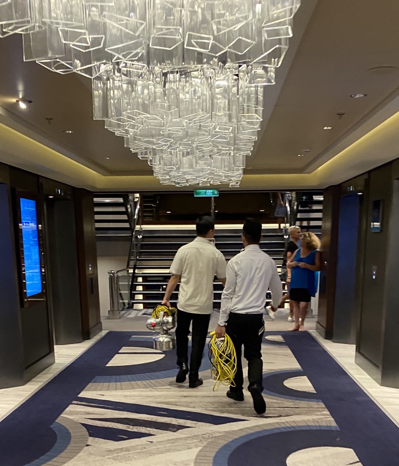 Crew members carrying defogging equipment in a hallway during a virus outbreak on a cruise ship.