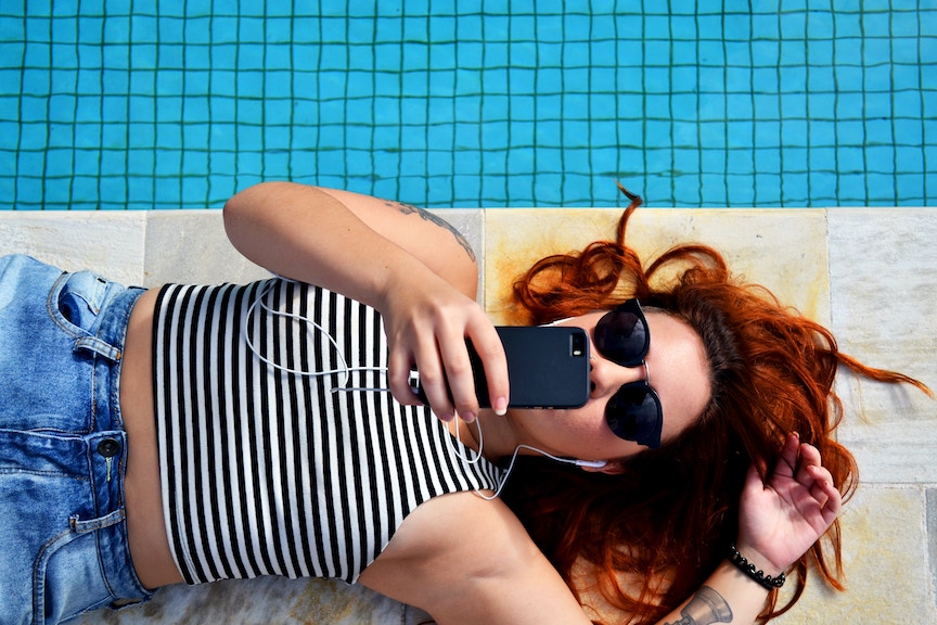 woman lying on the pool deck looking at her cell phone