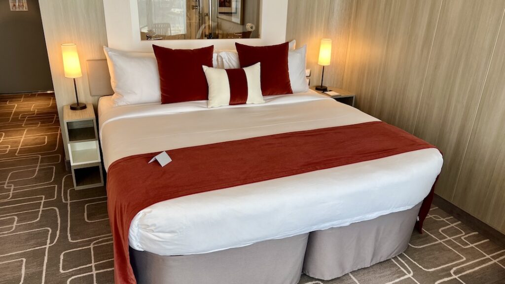 Cozy bedroom area in Celebrity Ascent Sky Suite, featuring a plush king-size bed flanked by stylish nightstands.