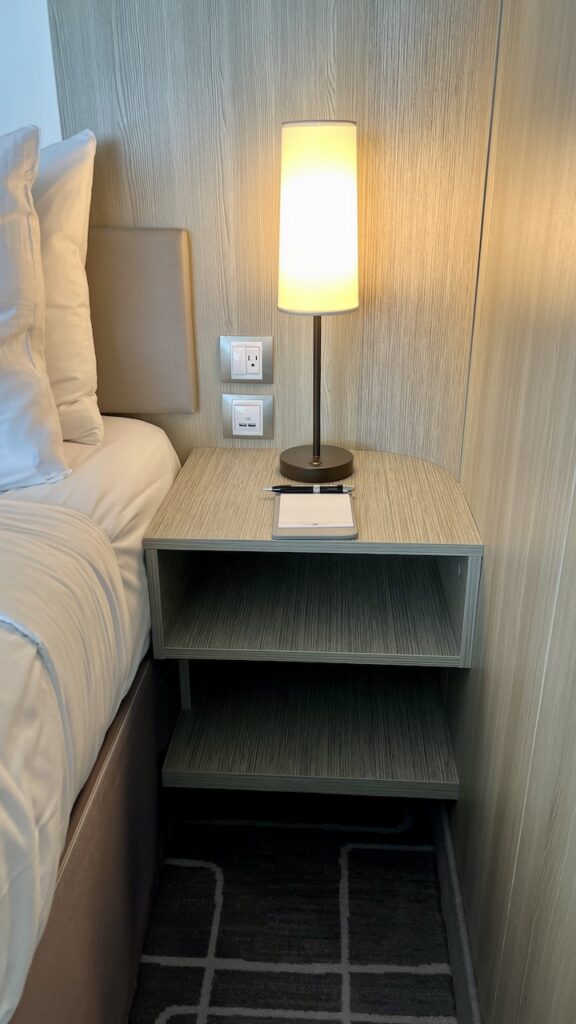 Right nightstand of the Sky Suite, wider with two cubbies and a tall, slim light affixed to its surface. One U.S. electrical outlet and two USB outlets.